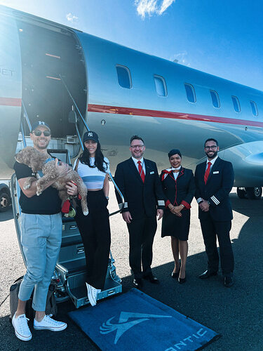 Couple with dog in front of private jet with crew.